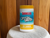 Container labeled 'Crystal Water O2 Shock' with a yellow lid on a white surface against a wooden background. Sulis Cleaner